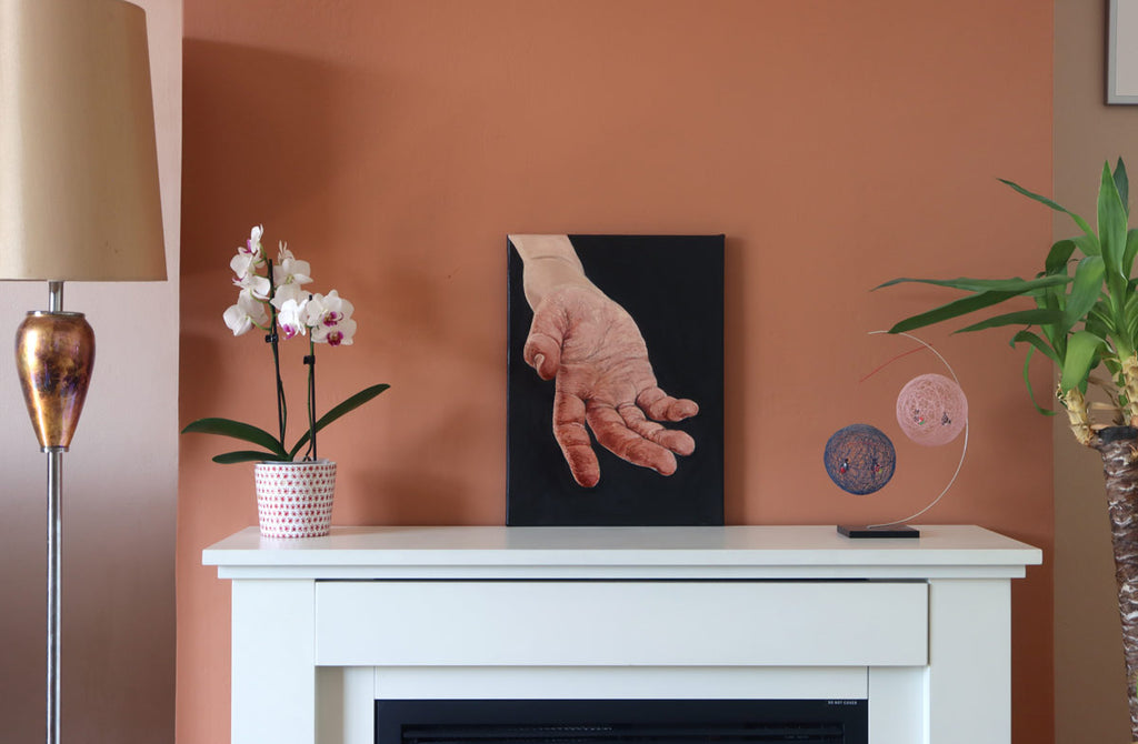 A photograph of an intimate 30 x 40 cm contemporary realism oil painting study of the human hand, showing scale and context, on our home mantlepiece.